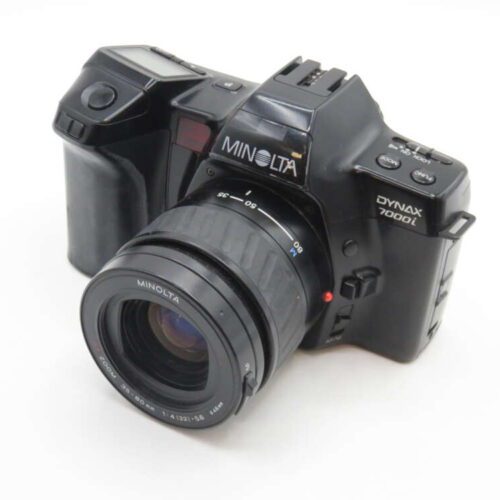 A Minolta Dynax 7000i film camera with a detachable zoom lens, resting on a white surface.