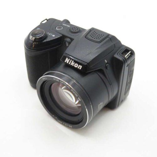 A Nikon digital camera with a large lens and optical zoom capability, resting on a white surface.