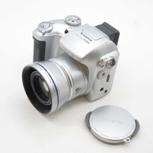 A silver Fujifilm FinePix S700 digital camera with a prominent lens, placed next to its detached lens cap on a white surface.