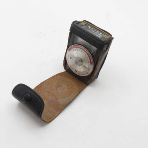 A vintage light meter with a round dial in a leather case, positioned open on a white background.
