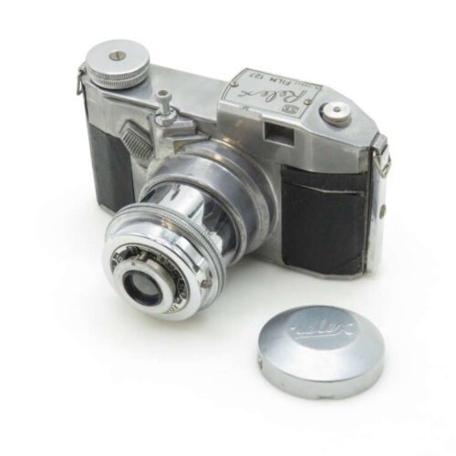A vintage metallic camera with a protruding lens and a cap placed beside it on a white surface.
