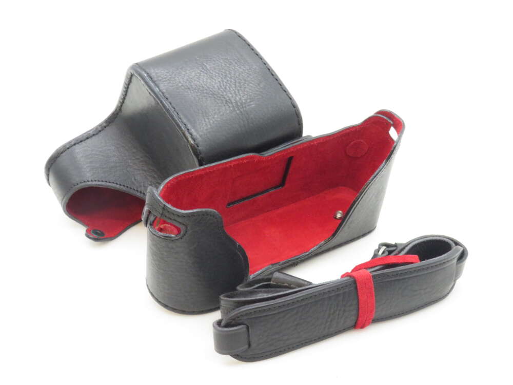 IMG_0679 Black leather camera case with a red interior and a matching black strap, displayed on a white surface.