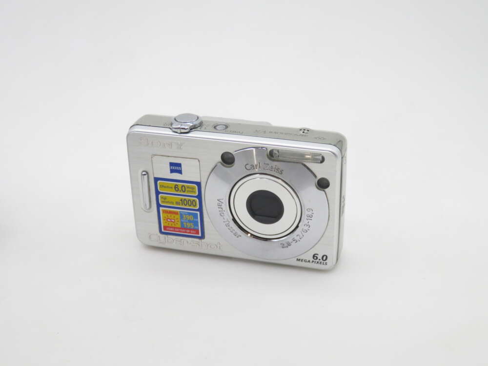 IMG_0762 A silver Sony Cyber-shot digital camera featuring a Carl Zeiss lens, 6.0 megapixels, and product stickers detailing features like effective ISO sensitivity and battery life.