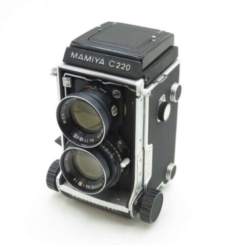 A vintage Mamiya C220 twin-lens reflex camera with a black and silver body, featuring two large lens openings on the front, a textured black covering, and a viewfinder on top.