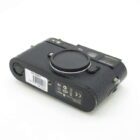 A black Leica M8 camera lying on its back with a body cap on, displaying various certification logos and a barcode sticker on the bottom surface.