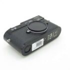 A black camera body with a textured grip, featuring a price tag and various certification symbols on the bottom. The lens is covered with a protective cap.