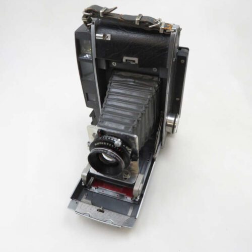 A vintage folding camera with a black leather bellows and metal body, featuring a lens and various knobs on a plain background.