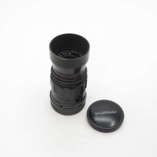 A black Voigtländer camera lens with its cap placed beside it on a white background.