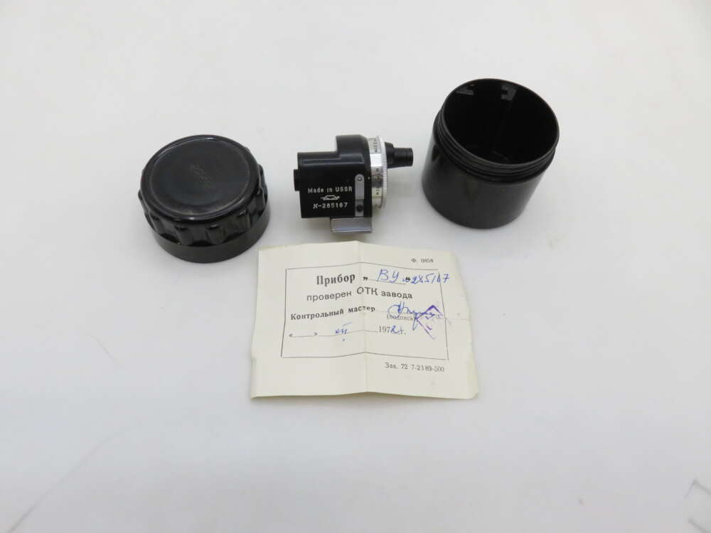 IMG_0979 A round black device with a label indicating 'Made in USSR' and the serial number, disassembled into three parts on a white surface, alongside a small piece of paper featuring text and handwriting in Russian.