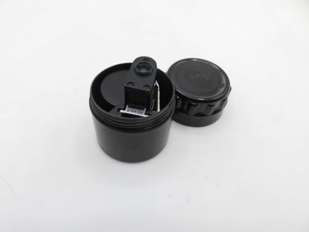 A black film canister with a detached lid and a piece labeled '24x36' inside, set against a white background.