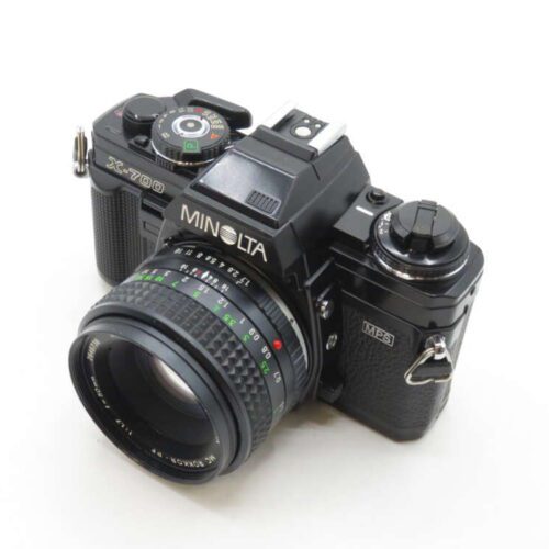 A black Minolta X-700 film camera with a 50mm MC Rokkor lens, featuring manual controls and a textured grip, positioned on a plain white background.