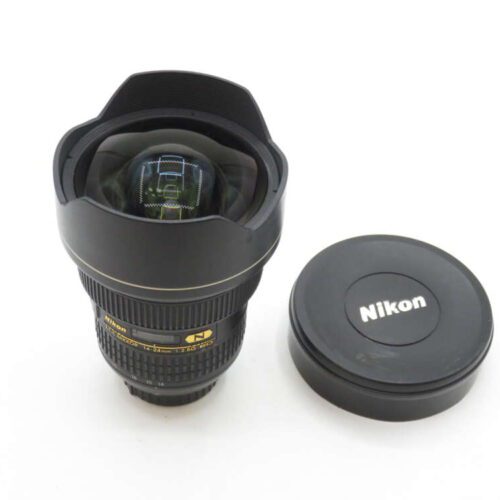A Nikon ultra wide-angle lens with a lens cap beside it, featuring a prominent front element and black exterior design with gold lettering.