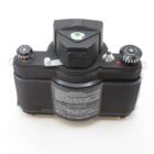 A vintage black camera viewed from the top, showing dials and a rectangular viewfinder, with instructional text in white on the back plate.