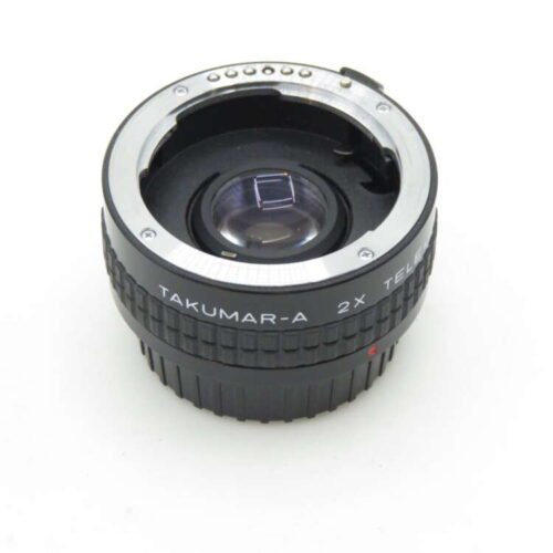 A Takumar-A 2x teleconverter lens with a black ribbed grip, featuring a metal mount and electronic contacts on the top surface, designed to connect with a camera lens system, displayed on a white background.