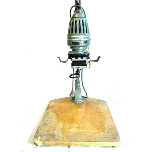 A vintage enlarger stands on a wooden base, featuring a metallic, vented lamp head with adjustment knobs and levers for photographic print processing.