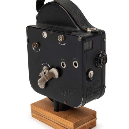 A vintage black Bolex movie camera with manual dials and a leather carrying handle, mounted on a wooden base.