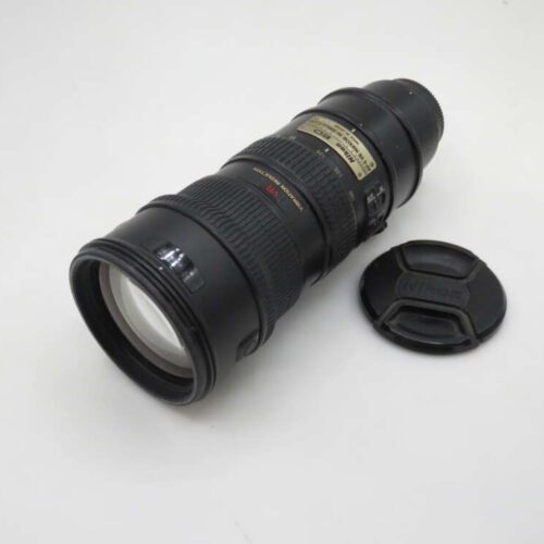 A Nikon telephoto camera lens with a black body, resting on its side next to a detached lens cap, on a white background.