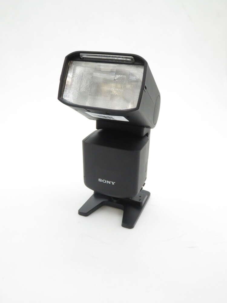 IMG_1187 A Sony external camera flash with a rectangular head and adjustable base, displayed on a white background.