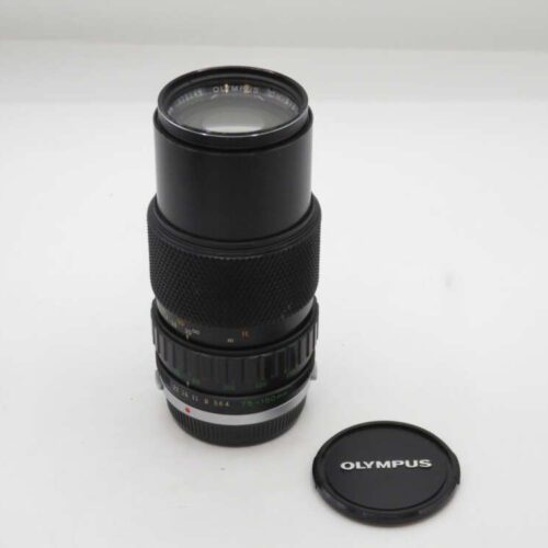 Olympus camera lens with a black body and an Olympus-branded lens cap placed beside it on a white surface.