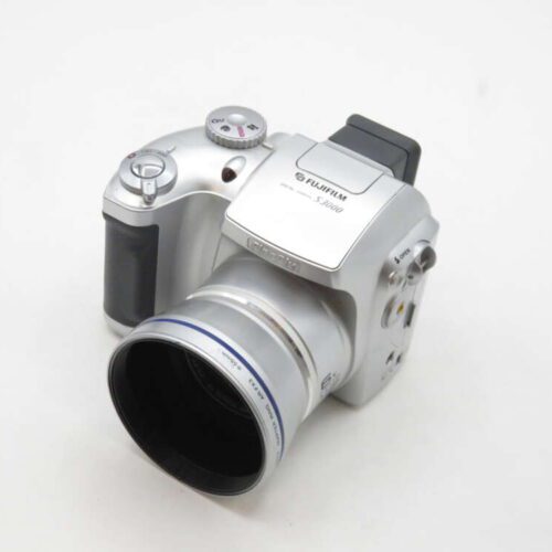 A silver Fujifilm FinePix S3000 camera with a rubber grip, featuring a large lens and control buttons on its top and side.