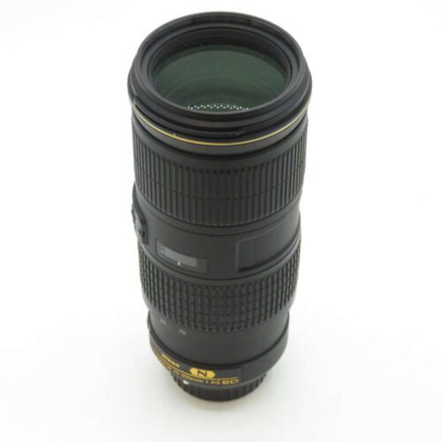 A black Nikon camera lens with a zoom ring and focusing ring, featuring gold lettering and markings, standing vertically on a plain white background.