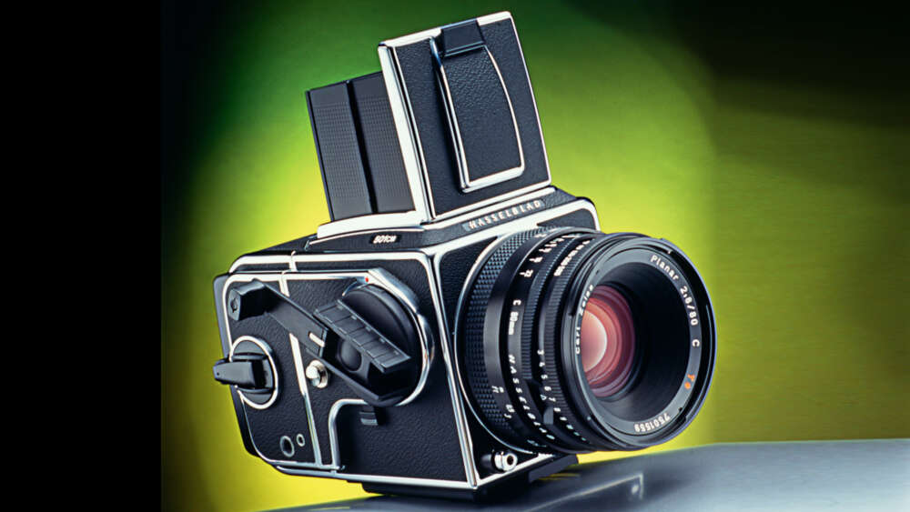 A classic medium format camera with a black body and a prominent lens, set against a gradient green and yellow background.