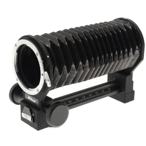 A Nikon camera bellows extension with a black accordion-like body and adjustment knobs, used for macro photography, mounted on a black rail with a scale.