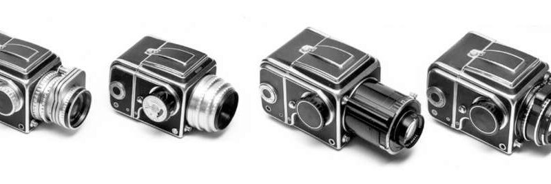 Four vintage Hasselblad 500 series cameras arranged in a row, each with a distinct lens attachment, shown in black and white.