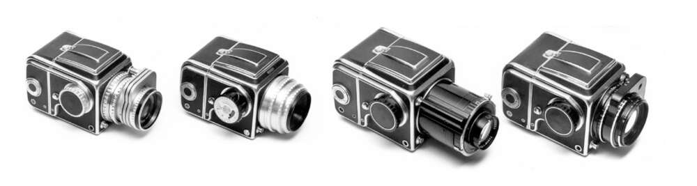 Four vintage Hasselblad 500 series cameras arranged in a row, each with a distinct lens attachment, shown in black and white.