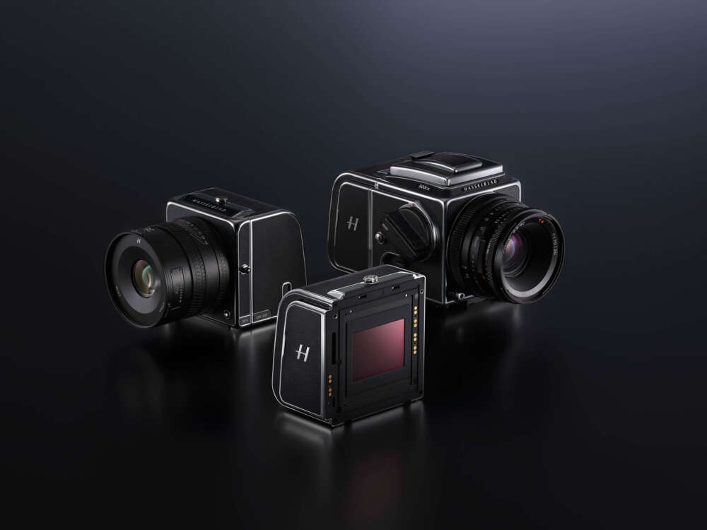 Three Hasselblad medium format camera bodies, two with lenses attached, displayed on a dark reflective surface.