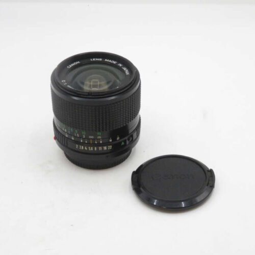 A Canon camera lens with a textured grip, displayed next to its detached lens cap on a plain white background.