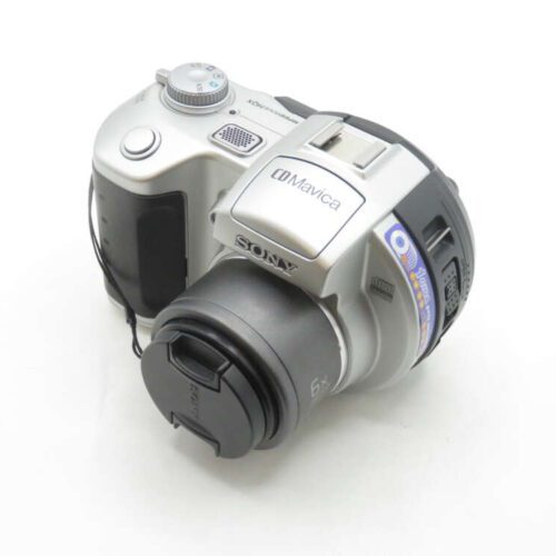 A silver Sony CD Mavica digital camera with a lens cap, shown from a top-side angle with control dials and a carrying strap visible.