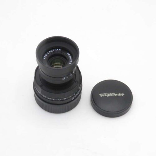 A Voigtländer 50mm f/3.5 APO-LANTHAR camera lens with its branded lens cap placed beside it on a white background.