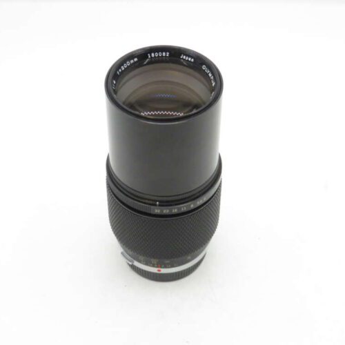 A black Olympus camera lens with a 300mm focal length, shown from an angle against a plain white background.
