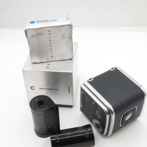 A Hasselblad camera magazine with its original packaging, alongside two black film cassettes, arranged on a plain background.