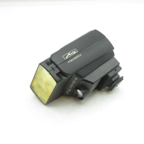 A Metz mecablitz 32 MZ-3 camera flash unit rests on a white surface, featuring a black plastic body with a yellow-tinted diffuser at the front.