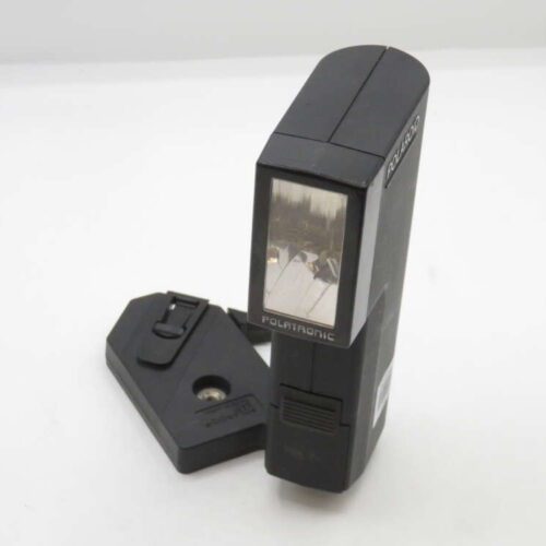 A black Polaroid flash attachment labeled "POLATRONIC" positioned upright on a white surface, with a separate black rectangular component placed next to it.