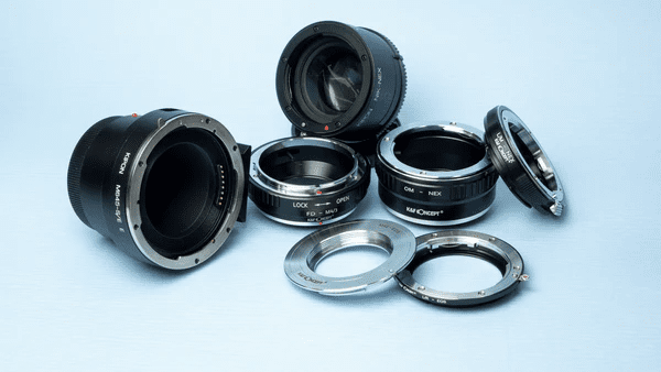A collection of camera lens adapters arranged on a light blue background, including various shapes and sizes such as cylindrical and ring-shaped models.