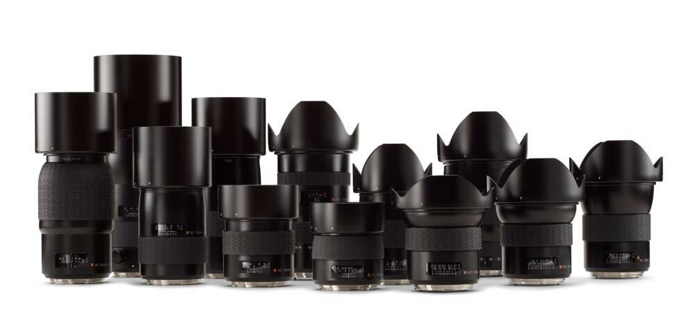 A collection of camera lenses arranged in two rows, showcasing various sizes and designs. The lenses are black and feature a mix of smooth and textured surfaces, with some having lens hoods attached.