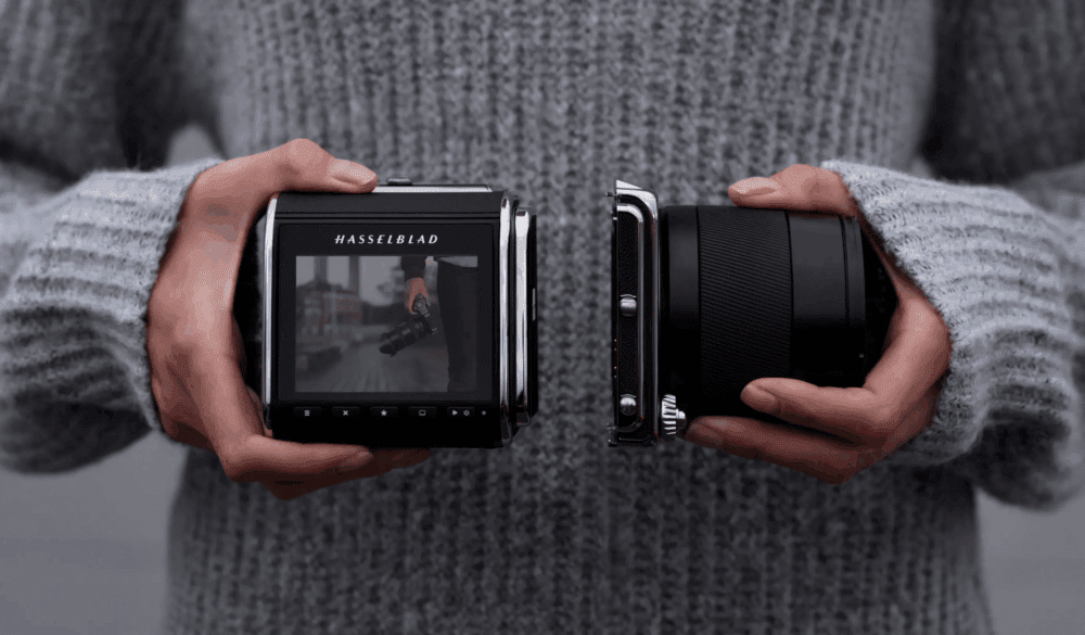 Person holding a camera with the lens and body separated, displaying a Hasselblad screen on the back showing a photo preview.