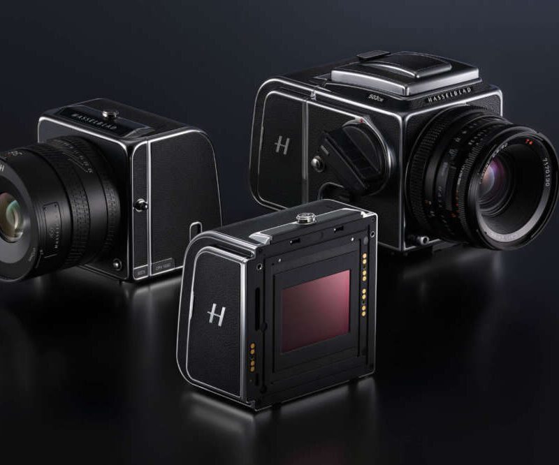 Three medium format cameras with black bodies and attached lenses displayed on a dark surface, showcasing a sleek, vintage design.
