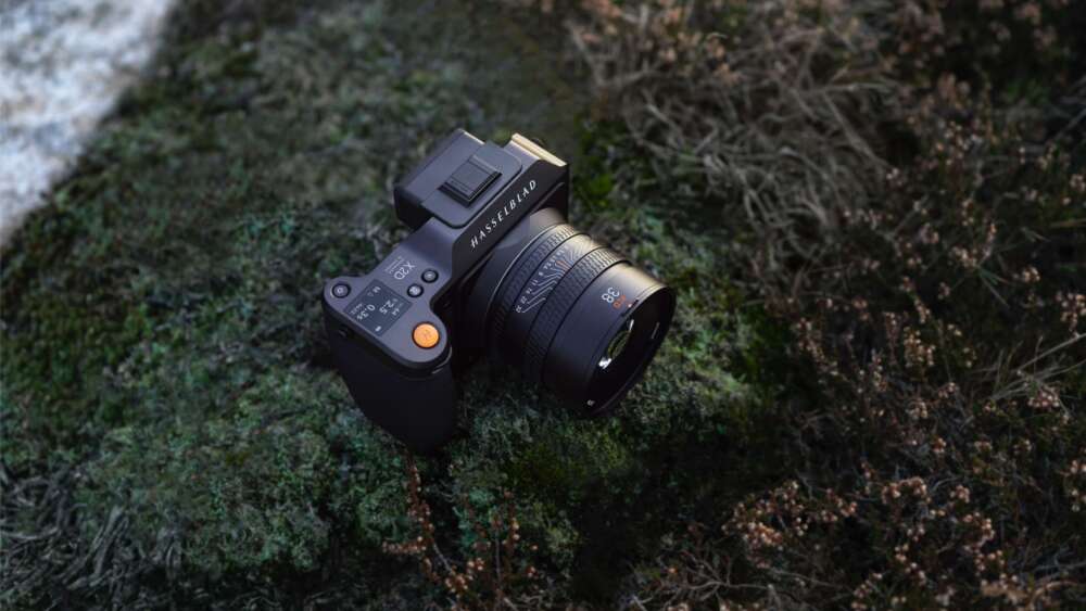 A professional camera with a lens attached, placed on a patch of green moss outdoors.