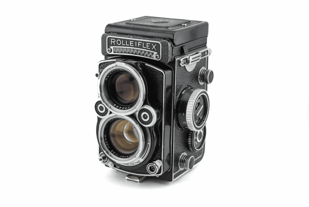 Close-up of a vintage Rolleiflex twin-lens reflex camera with a black and chrome finish, featuring two large lenses and various adjustment knobs on its side.