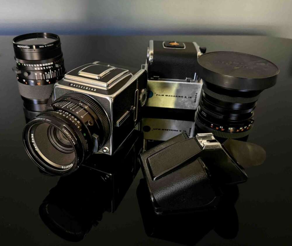 A Hasselblad camera with two interchangeable lenses and a film magazine on a reflective black surface.