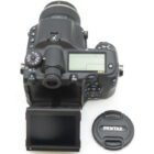 A Pentax 645Z DSLR camera with a flipped-out screen and a separate lens cap next to it on a white background.