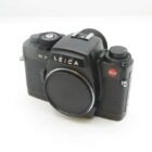 A Leica R7 film camera with a black body and lens cap attached, featuring textured grip panels and signature Leica branding on the front.