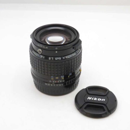 A Pentax 645 LS camera lens with a Nikon lens cap beside it on a white surface.