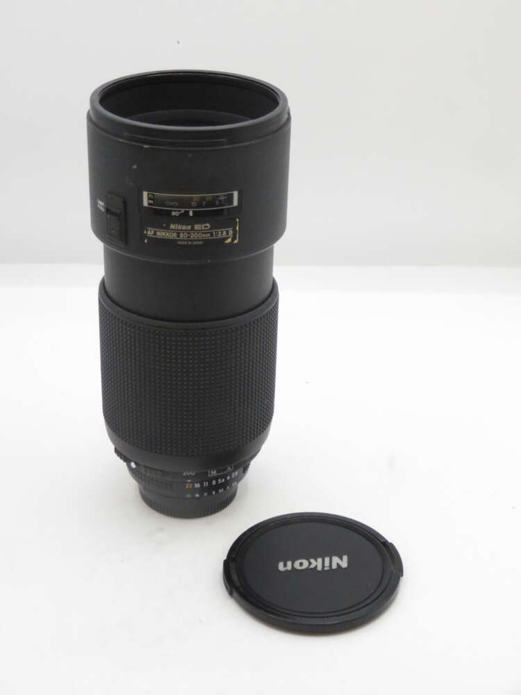IMG_1807 A Nikon ED AF NIKKOR 80-200mm lens with a black lens cap placed next to it on a white surface.