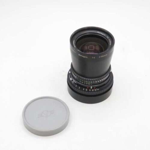 A Zeiss Distagon f/4 50mm camera lens with a black exterior, placed next to a grey lens cap on a white background.