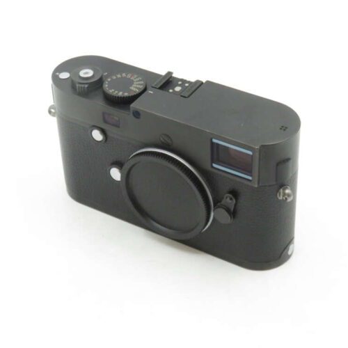 A black rangefinder-style camera with a body cap on the lens mount, featuring a textured grip and various control dials on the top.